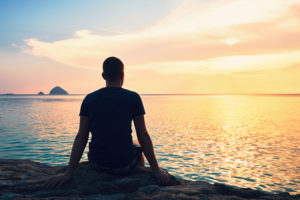 Rear view of person sitting on beach looking at sea at sunset 
