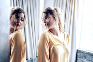 Person wearing loose blouse with long hair looks over shoulder at reflection in mirror