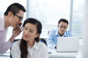 A concerned-looking office man watches two coworkers whispering.