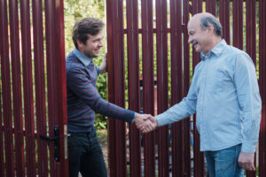 One man leans through a gate to shake another man's hand.