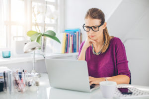 Person with glasses and serious expression works on computer in home office