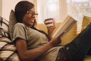 Person sitting on the sofa reads while drinking from brown and white mug