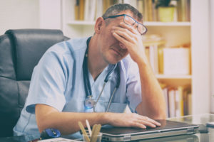 A middle-aged doctor frowns and covers his face.