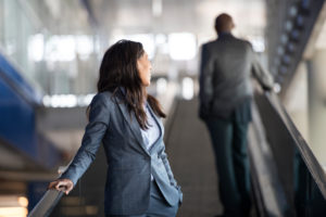 Person with long hair leans back on escalator rail looking at back of colleague in suit
