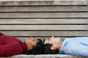 Couple lying head to head on their backs on bench, looking up thoughtfully at sky