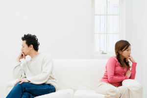 Two partners sit on opposite sides of sofa looking away from each other