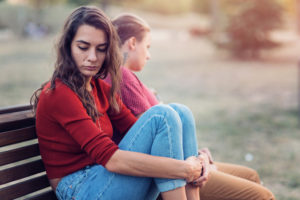 Two young adults sit on bench, space between them, looking away from each other