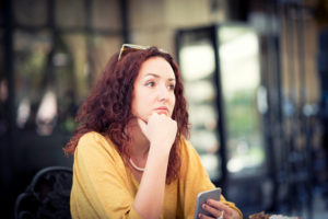 Person sits at table with chin resting on hand, holding phone and staring off into distance
