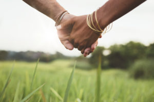 Close-up shot of two joined hands over tall grass in field