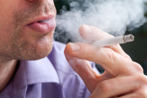 A closeup of a man breathing out cigarette smoke