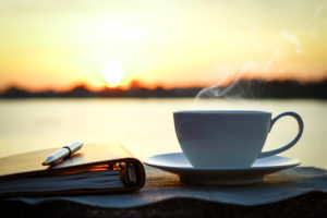 Coffee, journal, and pen on table outside at sunrise