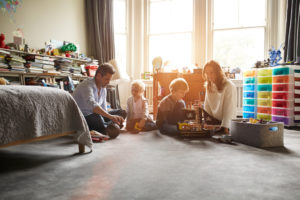 Two parents sitting apart and not talking interact with young children in a child's bedroom