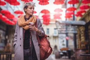 Young androgynous adult holding coffee looks down street in town