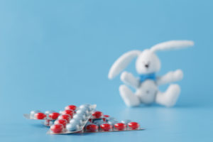 Two packs of red and white pills lie on the ground. A toy rabbit sits out of focus.