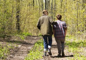 Rear view of parent and youth walking on trail in woods and talking