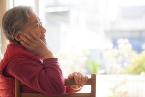 Senior adult with short hair sits at table, face resting on hand, looking into distance thoughtfully