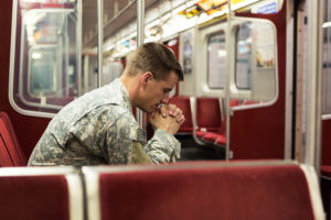 A soldier sits in an empty train car, looking deep in thought.
