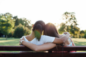 Rear view of parent and teenager, both with long hair, sitting on bench