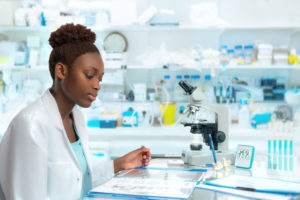 A young graduate student is working in a laboratory. A microscope sits in front of her.