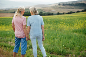 Two older adults stand in field holding hands, happy together