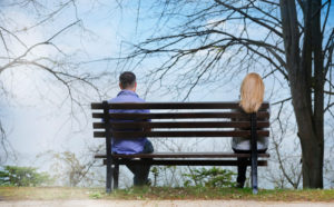 Rear view of couple sitting apart from each other on bench underneath tree 
