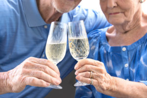 Close-up of an aged couple holding champagne flutes. They are both wearing blue shirts.