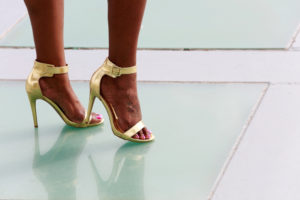 A woman with golden high heels stands atop a green tile floor.