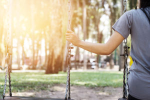 Arm of person who is sitting on swing alone reaches to hold chain of other swing