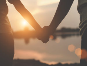 Close-up photo of loving couple holding hands while walking at sunset