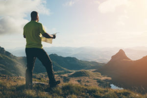 Man with a map standing on top of the mountain, looking ahead.