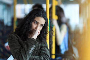 Person with long, curly dark hair holds hand to mouth thoughtfully while riding train home
