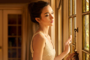 Young adult with hair pulled back stands with palm on windowed door, looking out