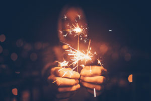 A close-up of sparklers in a man's hand. The man's face is out of focus.