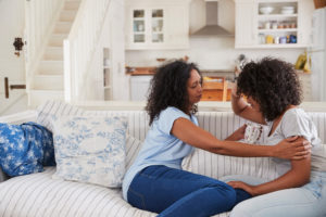 Mother talking to upset daughter on sofa in living room