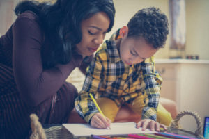 Mother looking over son's shoulder while he colors