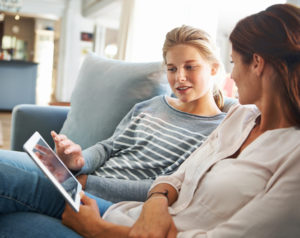 Mom and teenager sit on sofa, looking at tablet together