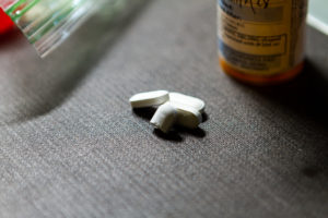 A photo of white pills on the floor next to a prescription bottle and a ziplock bag.