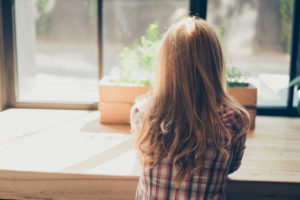 Rear view of person with long, wavy hair sitting at empty table looking out window