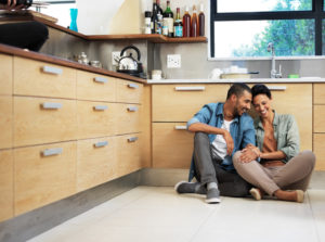 Couple looking happy together sit on kitchen floor talking together and smiling