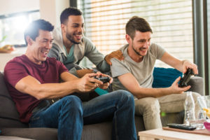 Three men play a video game in a sunny room. 