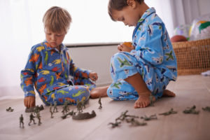 Two young children in pajamas play on their bedroom floor with toy soldiers