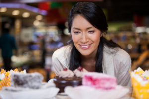 Happy woman selecting desserts from display in supermarket