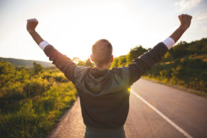 Rear view of person on road raising arms to the sky 