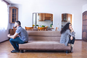Partners sit on opposite ends of sofa, turned in opposite directions and facing away from each other