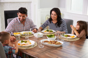 Two parents and two children sit down at the table to enjoy a meal together, talking and smiling