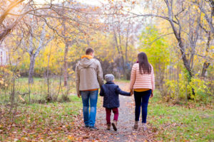 Rear view photo of two parents and child walking along path in park in autumn