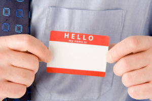A close up of hands attaching a blank name tag next to a blue tie.