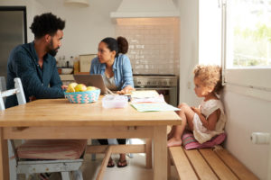 Young child sits back on bench looking up at parents who are having an intense discussion and seemed stressed