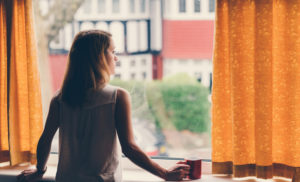 Thoughtful woman at home looking through the window at the street outside