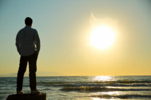 A man stands with his hands in his pockets, overlooking the ocean waves.